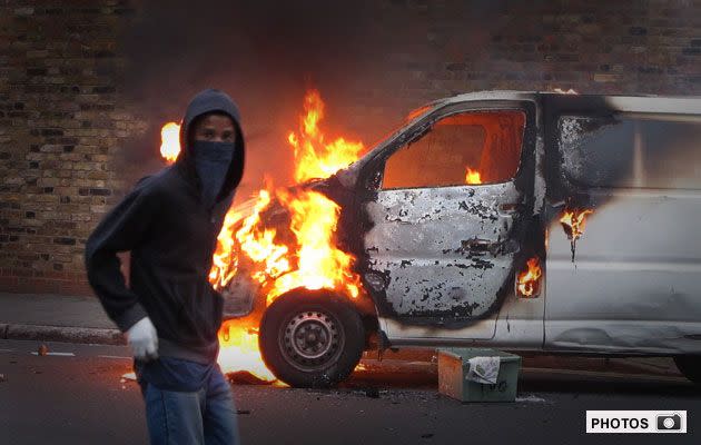 A hooded youth walks past a burning vehicle in Hackney. Photo: Getty Images