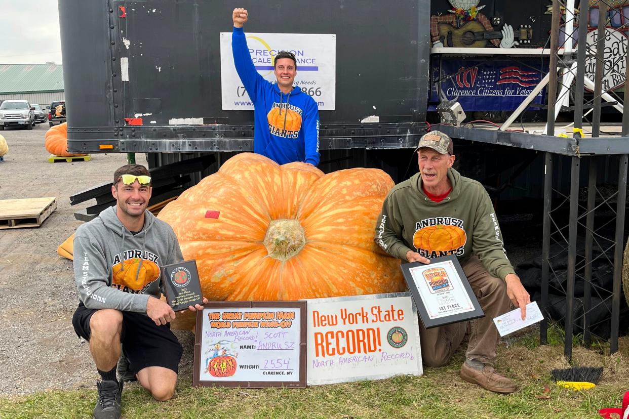 Emmett Andrusz, from left, Steve Andrusz and Scott Andrusz, pose with the record setting 2,554-pound pumpkin, in Clarence, N.Y., Saturday, Oct. 1, 2022. Scott Andrusz's entry broke the previous record of 2,528 pounds. 