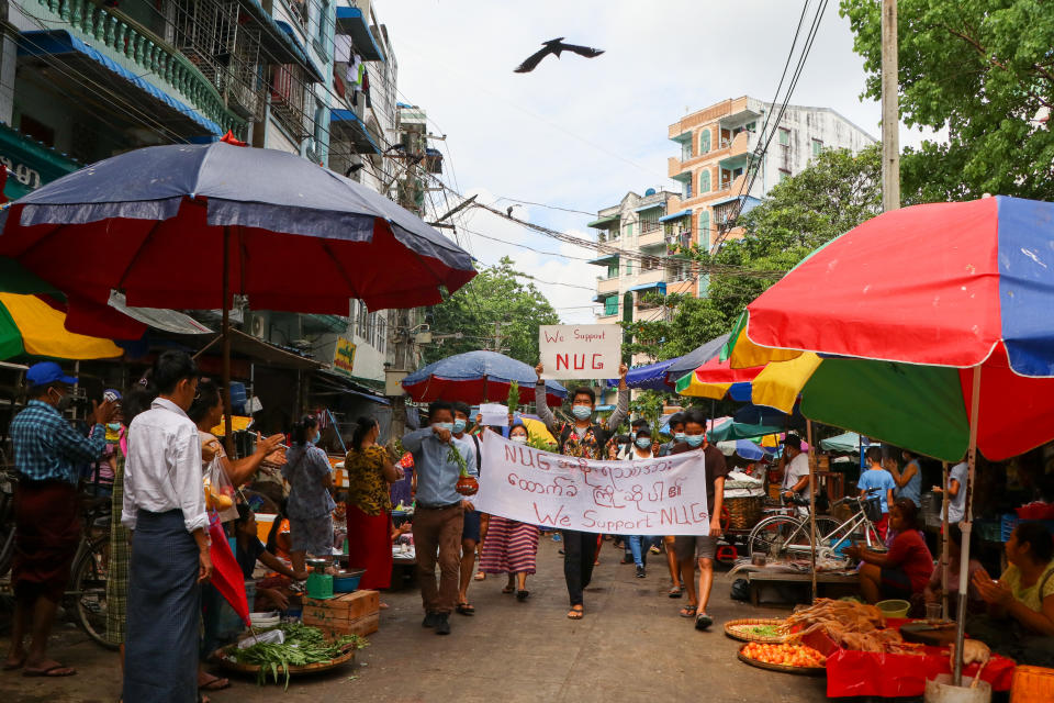 Anti-coup protesters hold signs that read "We Support NUG" that stands for ‘national unity government’ as they march on a street where vendors sell fresh products Saturday, April 17, 2021 in Yangon, Myanmar. Opponents of Myanmar’s ruling junta have declared they have formed an interim national unity government with members of Aung San Suu Kyi’s ousted cabinet and major ethnic minority groups.. (AP Photo)