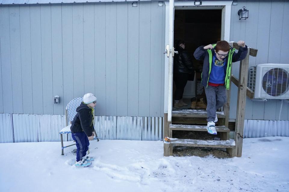 Hunter Prince, right, leaps out of his family's temporary home into the snow as his brother, Waylon, watches, Tuesday, Jan. 16, 2024, in Water Valley, Ky. Two years after the tornado outbreak that killed dozens and leveled much of the real estate in Mayfield, many people, like the Prince family, are still living through another, slower disaster, the search for housing. (AP Photo/Joshua A. Bickel)