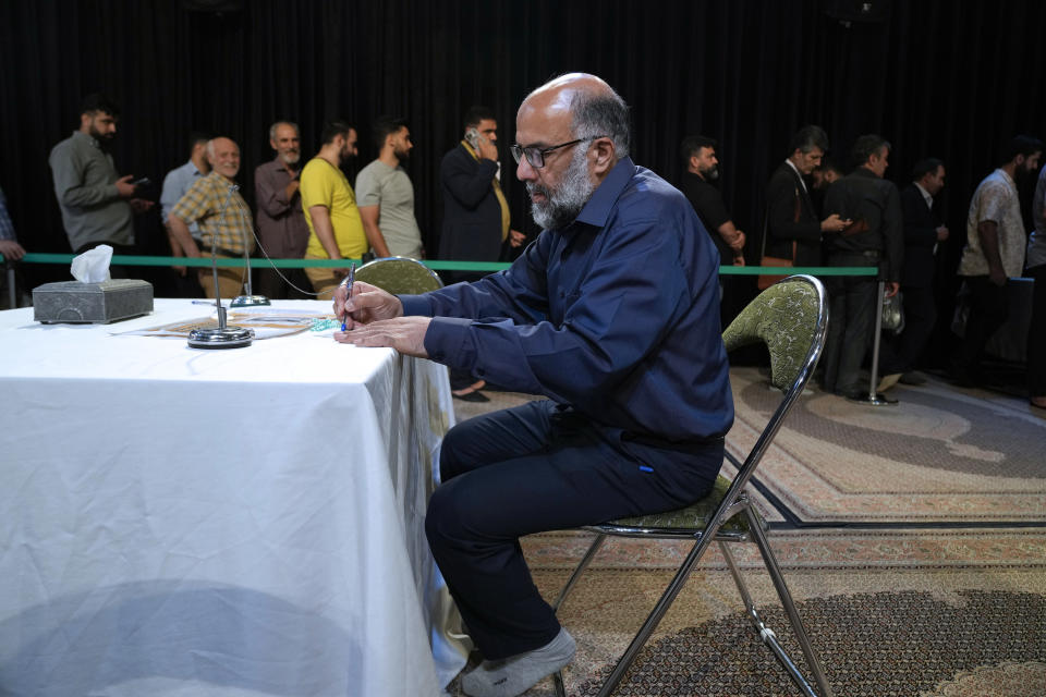 A man fills out his ballot as others line up during the presidential election in a polling station at the shrine of Saint Saleh in northern Tehran, Iran, Friday, July 5, 2024. Iran held a runoff presidential election that pitted a hard-line former nuclear negotiator against a reformist lawmaker. (AP Photo/Vahid Salemi)