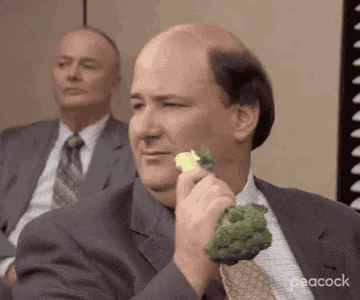 Kevin from "The Office" holds a broccoli floret to his face and takes a bite.