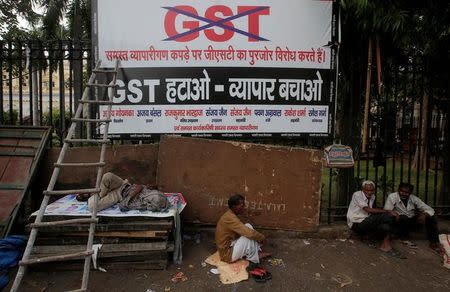Labourers sit next to a banner after a protest against the implementation of the goods and services tax (GST) on textiles, in the old quarters of Delhi, June 29, 2017. The banner reads “Remove GST – save business”. REUTERS/Adnan Abidi