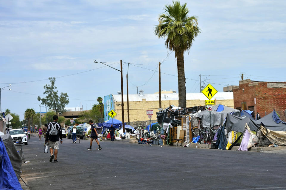 FILE - People walk through "The Zone," a homeless encampment, July 11, 2023, in Phoenix. Homeless people are among the people most likely to die in the extreme heat in Phoenix. (AP Photo/Matt York, File)