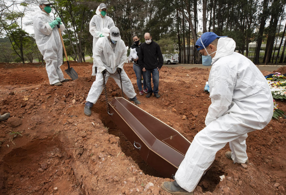 Darick Caverni and his wife Michelle watch as cemetery workers in protective clothing lower the coffin that contain the remains of his 88-year-old aunt Wilma Caverni, who died of the new coronavirus, at the Vila Formosa cemetery in Sao Paulo, Brazil, Wednesday, July 15, 2020. Brazil is nearing 2 million cases of COVID-19 and 75,000 deaths. (AP Photo/Andre Penner)