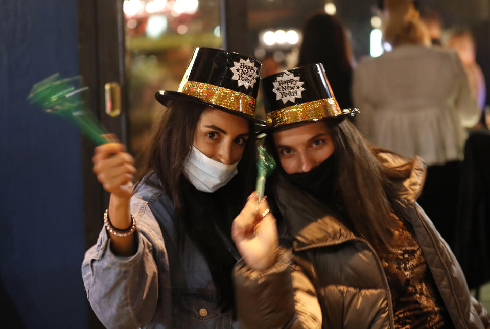 Lebanese women wearing protective masks to prevent the spread of the coronavirus, celebrate the New Year outside a pub, in Beirut, Lebanon, early Friday, Jan. 1, 2021. Lebanon ended the year with more than 3,500 newly registered infections of coronavirus and 12 new deaths as its health minister appealed to Lebanese to take precautions while celebrating to avoid what he called wasting sacrifices made in combatting the virus. (AP Photo/Hussein Malla)