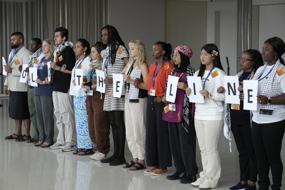 Activistas muestran carteles que forman la frase "mantengan la línea" cerca del secretario general de Naciones Unidas, António Guterres, mientras habla en durante una conferencia de prensa en la cumbre climática de la ONU COP28 en Dubái, Emiratos Árabes Unidos, el lunes 11 de diciembre de 2023. (AP Foto/Peter Dejong)