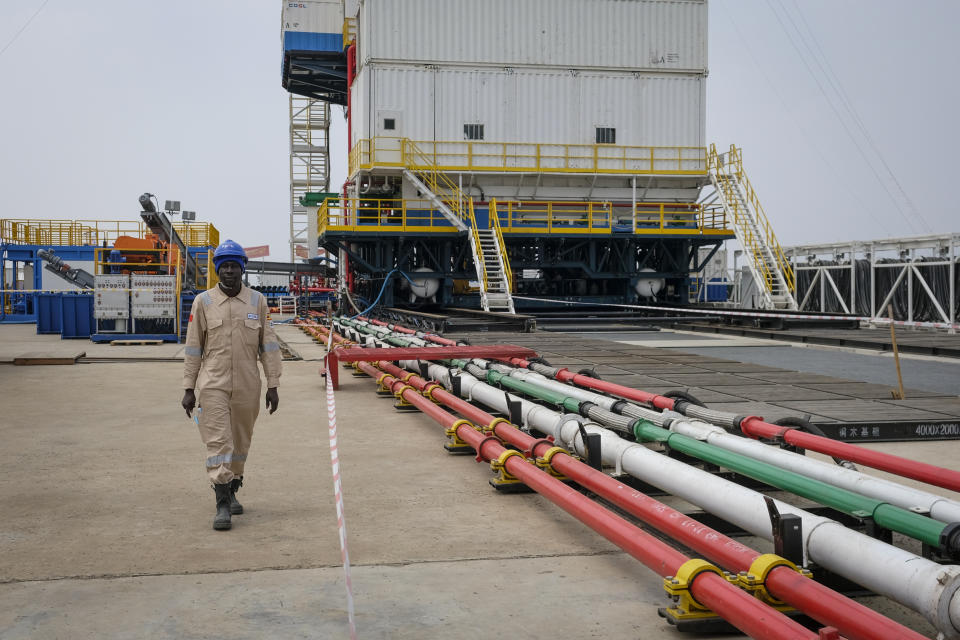 FILE - A Ugandan worker from China Oilfield Services Limited (COSL), a contractor for China National Offshore Oil Corporation (CNOOC), walks by pipes near the drilling rig at the Kingfisher oil field on the shores of Lake Albert in the Kikuube district of western Uganda Tuesday, Jan. 24, 2023. (AP Photo/Hajarah Nalwadda, File)