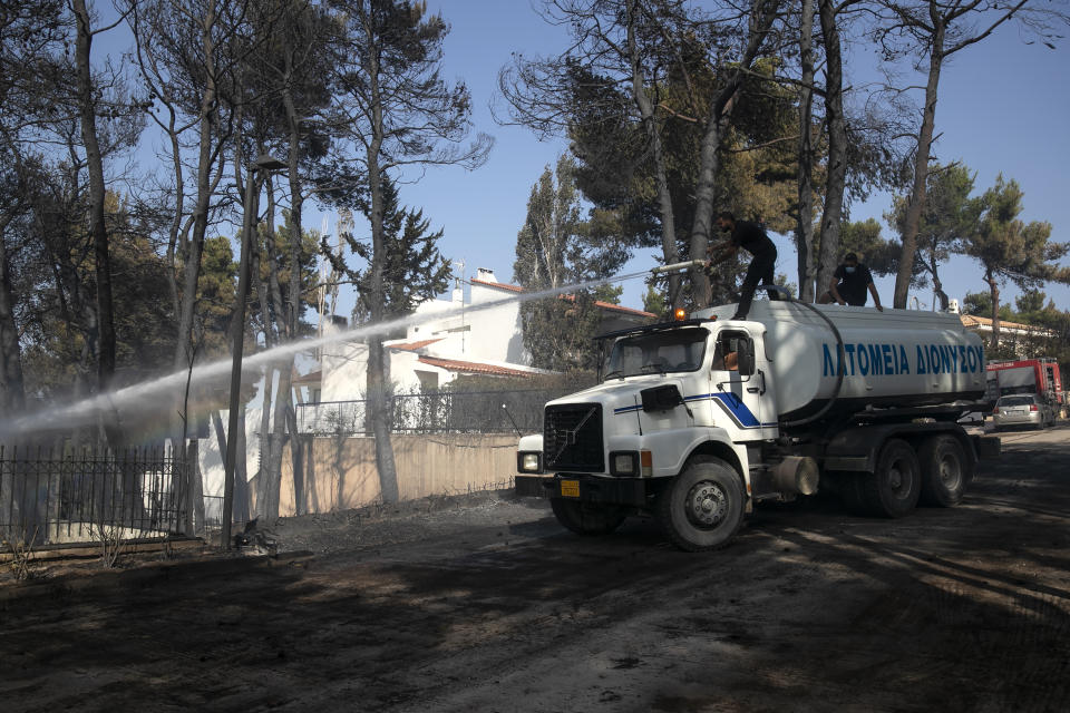 Municipal workers spray water during a forest fire at Dionysos northern suburb of Athens, on Tuesday, July 27, 2021. Greek authorities have evacuated several areas north of Athens as a wildfire swept through a hillside forest and threatened homes despite a large operation mounted by firefighters. (AP Photo/Yorgos Karahalis)