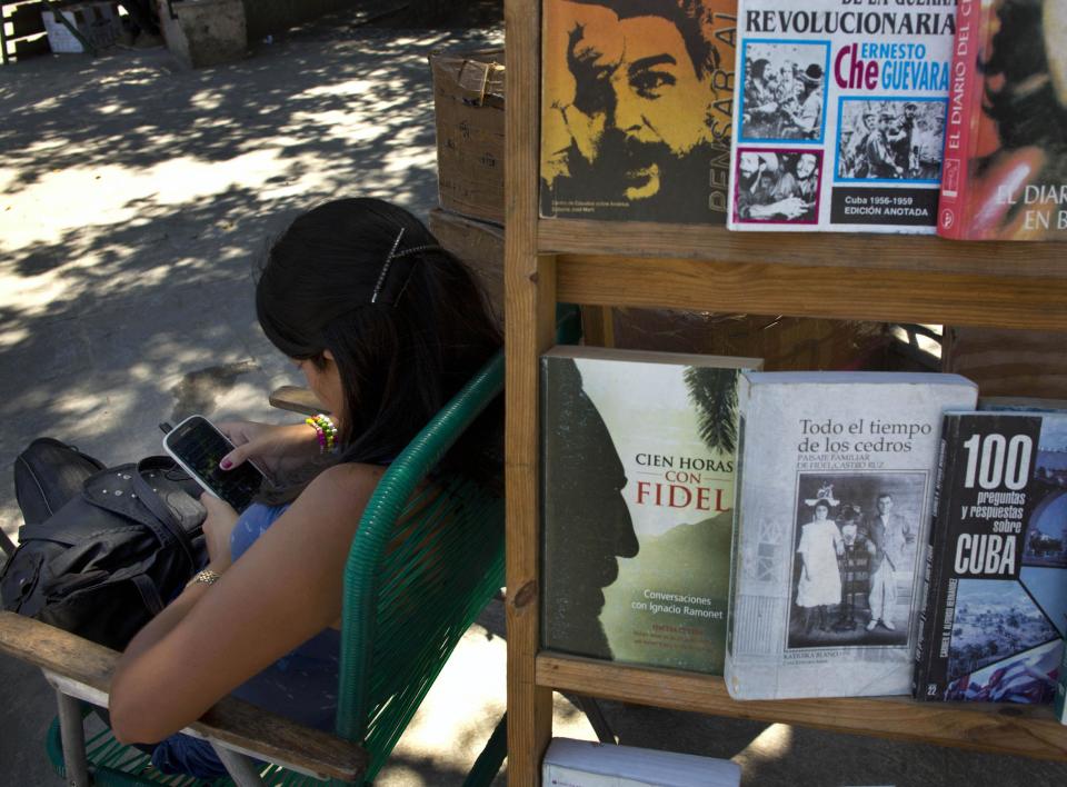 A book street vendor passes the time on her smart phone as she waits for customers in Havana, Cuba, Tuesday, April 1, 2014. The Obama administration secretly financed a social network in Cuba to stir political unrest and undermine the country’s communist government according to an Associated Press investigation. The project, dubbed "ZunZuneo," slang for a Cuban hummingbird’s tweet, lasted more than two years and drew tens of thousands of subscribers and sought to evade Cuba’s stranglehold on the Internet with a primitive social media platform. First, the network would build a Cuban audience, mostly young people; then, the plan was to push them toward dissent. (AP Photo/Ramon Espinosa)