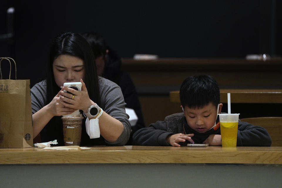 Una mujer y un niño revisan sus teléfonos celulares en un café en Beijing, el 19 de enero de 2023.Al aproximarse las festividades del Año Nuevo Lunar en China con promesas de banquetes y sobres rojos llenos de dinero, los niños anhelan algo más: una hora extra para jugar en internet cada día. (Foto AP/Andy Wong)