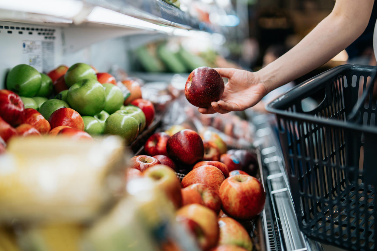 Cropped shot of young Asian woman choosing fresh organic fruits in supermarket. She is picking a red apple along the produce aisle. Routine grocery shopping. Healthy living and eating lifestyle