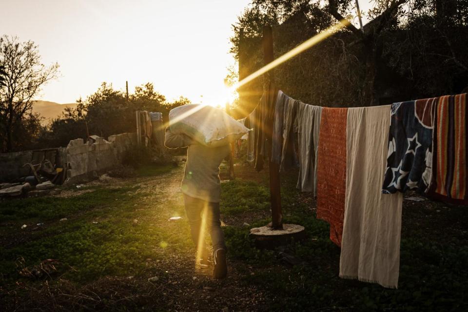 A man walking toward the setting sun, past a clothesline of drying laundry, with a full bag on his shoulder