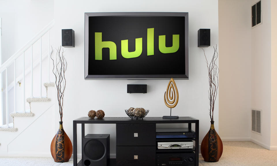 A living room with a TV hanging on the wall which says 'Hulu' on it in green writing. There's a TV cabinet underneath the TV with ornaments.