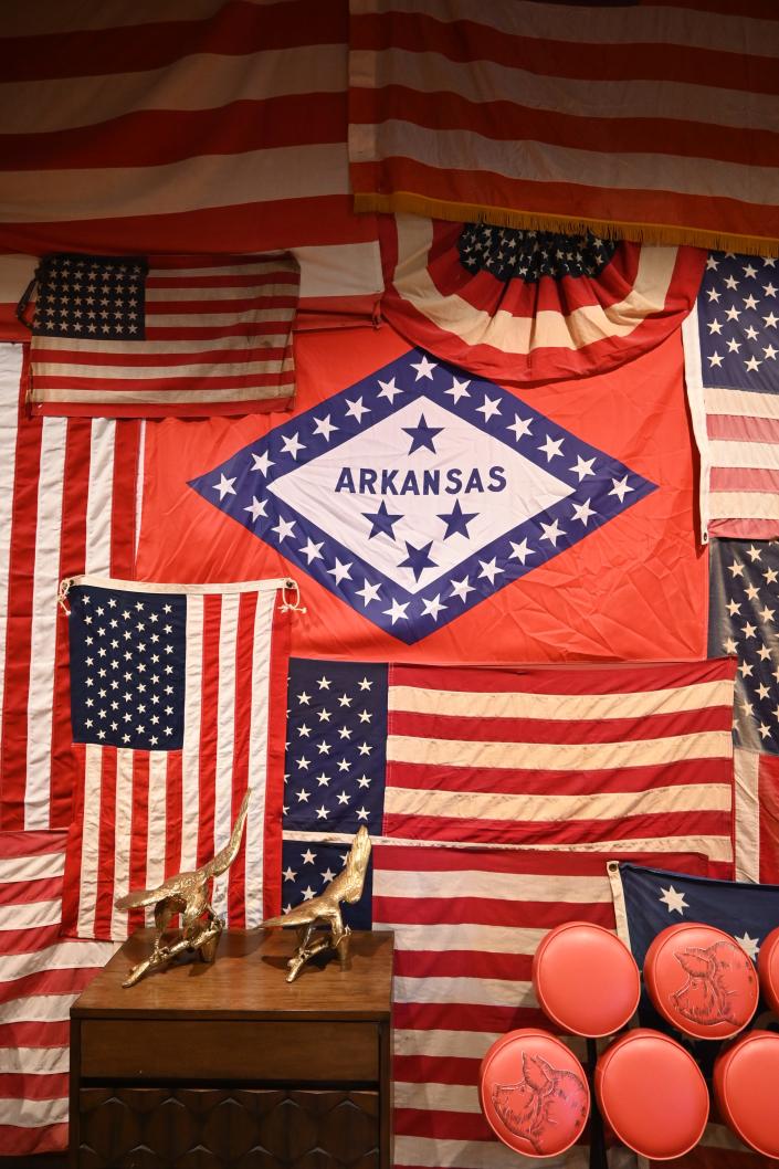 A wall display of an Arkansas flag surrounded by United States flags.