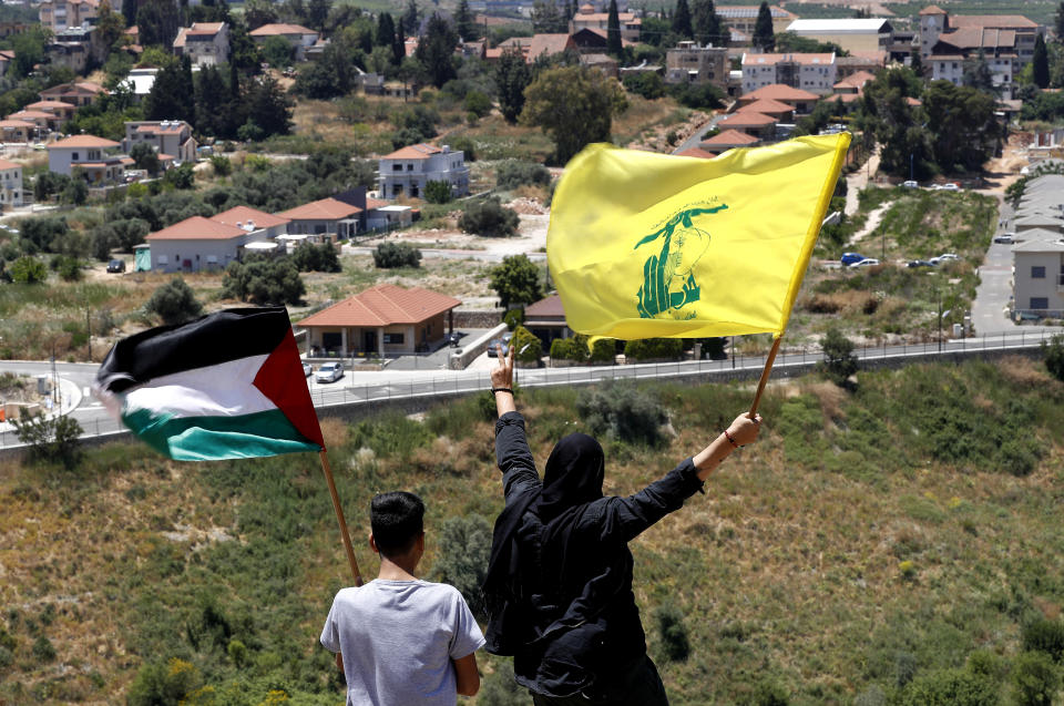 FILE - In this May 15, 2021, file photo, Lebanese wave Hezbollah and Palestinian flags, as they stand in front of the Israeli town of Metula, background, on the Lebanese side of the Lebanese-Israeli border in the southern village of Kfar Kila, Lebanon. Lebanon's Hezbollah militia looms large over the current Israel-Hamas war, even though it has stayed out of the fighting so far. Hezbollah's firepower is far greater than that of Gaza's Hamas rulers, and Israel keeps a wary eye on its northern border for any signs Hezbollah might get off the sidelines. (AP Photo/Hussein Malla, File)