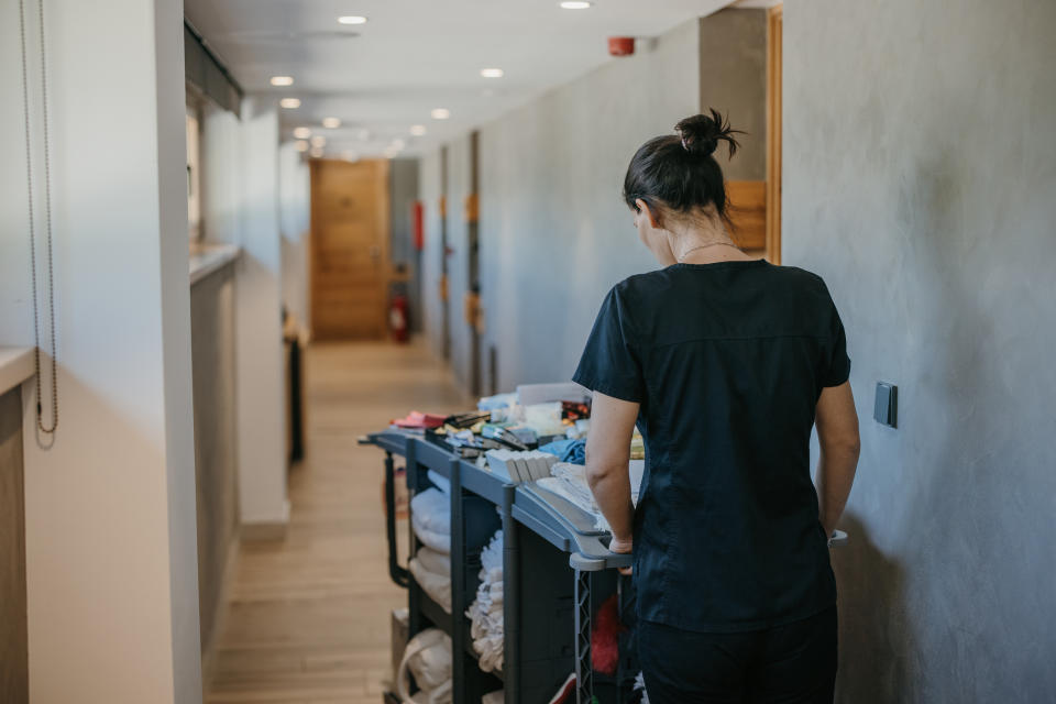 Person in a work uniform stands behind a housekeeping cart in a hotel hallway