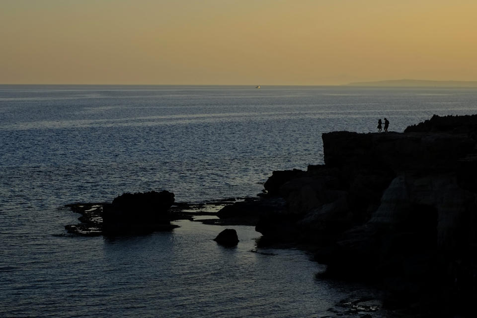 A couple tourists in silhouettes visit the sea caves at sunset, in the southern coastal resort of Ayia Napa in southeast Mediterranean island of Cyprus, Sunday, May 29, 2022. Hundreds of Russian and Ukrainian Orthodox faithful visiting Cyprus would stream daily past the icon of the Virgin Mary at Kykkos Monastery to venerate the relic that tradition dictates was fashioned by Luke the Evangelist and blessed by the Virgin herself. But a European Union ban on flights to and from Russia as a result of Russia's invasion of Ukraine has meant a loss of 800,000 vacationers - a fifth of all tourists to Cyprus in record-setting 2019. (AP Photo/Petros Karadjias)