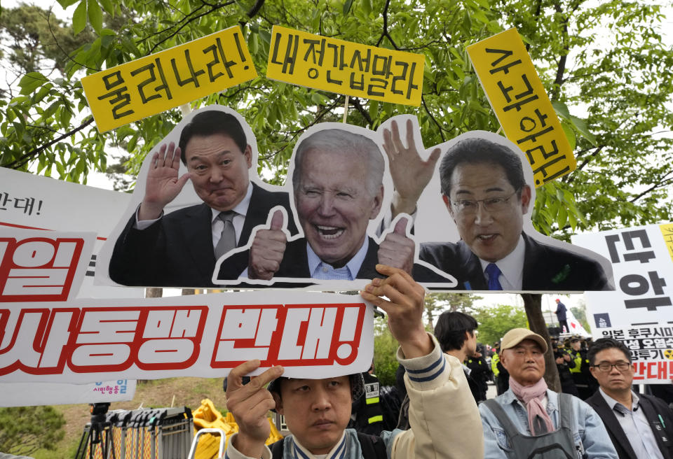 A protester holds up images of South Korean President Yoon Suk Yeol, left, U.S. President Joe Biden and Japanese Prime Minister Fumio Kishida, right, during a rally to oppose a visit by Kishida in front of the presidential office in Seoul, South Korea, Sunday, May 7, 2023. The leaders of South Korea and Japan are to meet Sunday for their second summit in less than two months, as they push to mend long-running historical grievances and boost ties in the face of North Korea's nuclear program and other regional challenges. (AP Photo/Ahn Young-joon)