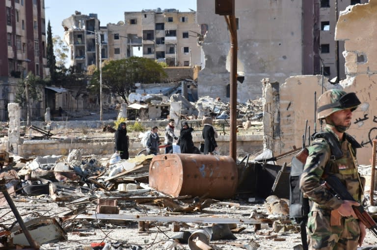 Syrians walk amid debris as a soldier secures the Masaken Hanano neighbourhood in Aleppo, on December 6, 2016