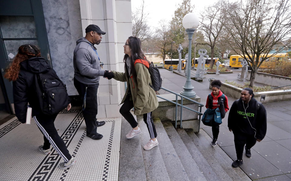 Teaching assistant Leonardo Baker, left, greets students arriving at Franklin High School Wednesday morning, Dec. 12, 2018, in Seattle. The Seattle School District changed from a 7:50 a.m. start time to 8:45 a.m. in the fall of 2016 for high schools and most middle schools, joining dozens of other U.S. school districts adopting later starts to fight teen sleep deprivation. (AP Photo/Elaine Thompson)