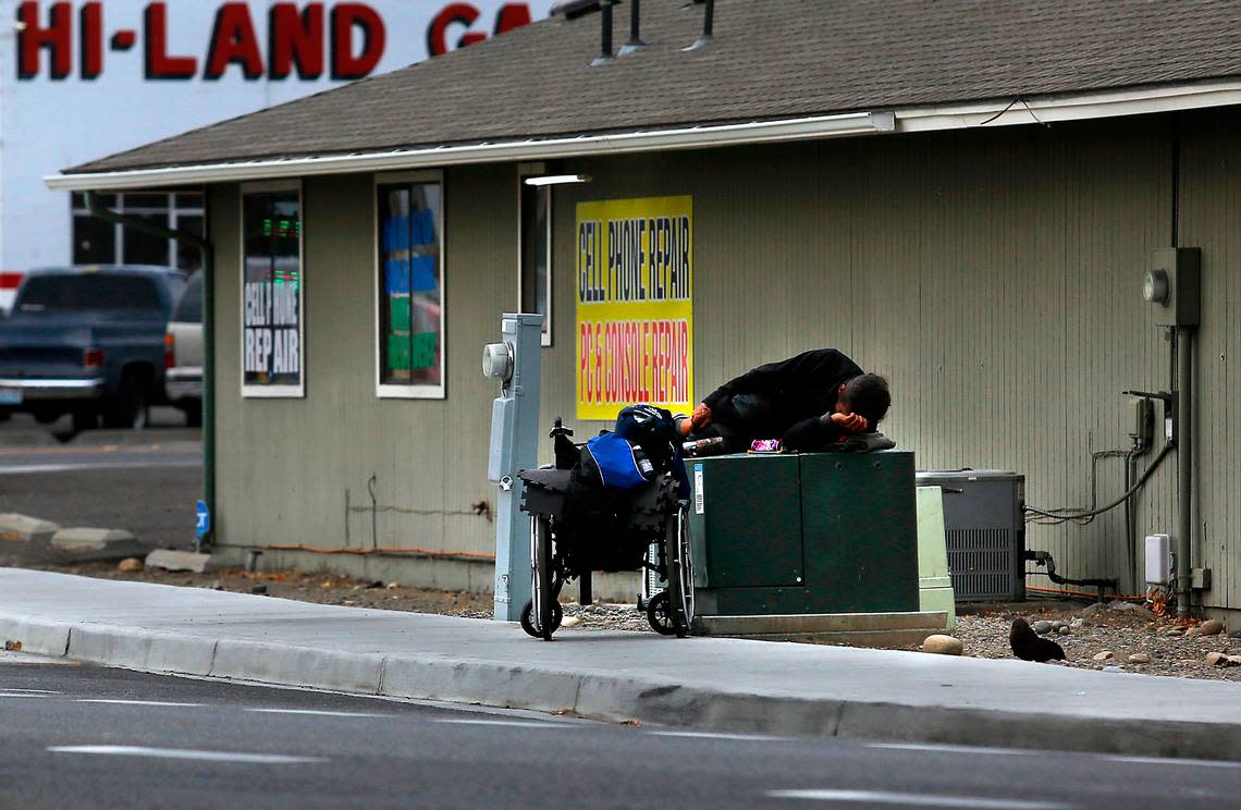 A man sleeps on a metal electrical box with his wheelchair and belongings nearby in September 2022 on Union Street near Clearwater Avenue in Kennewick.