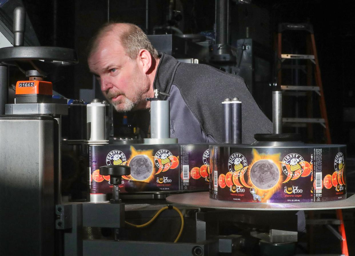 Thirsty Dog Brewing Company co-owner John Najeway eyes Solar Eclipse Vienna lager labels being fixed to moving along the canning line on March 21.