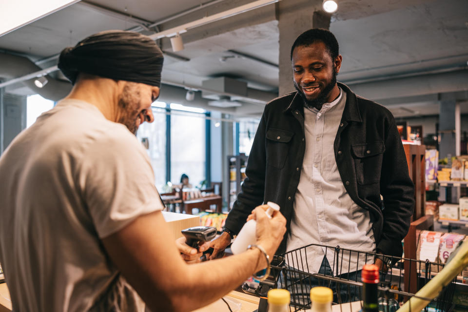 Two men interacting in a grocery store, one scanning items while the other observes