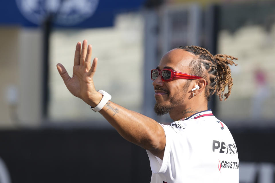 FILE - Mercedes driver Lewis Hamilton of Britain, waves as he arrives for the F1 drivers group picture ahead the drivers parade prior to the Abu Dhabi Formula One Grand Prix at the Yas Marina racetrack in Abu Dhabi, United Arab Emirates, Sunday, Nov. 26, 2023. Driving for Ferrari next year will be a dream come true for Lewis Hamilton but the seven-time Formula One champion remains “100% committed” to Mercedes until then, he wrote Saturday, Feb. 3, 2024. (AP Photo/Kamran Jebreili, File)