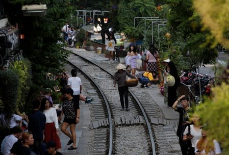 A vendor walks on a railway track as tourists gather on either side, in the Old Quarter of Hanoi, Vietnam