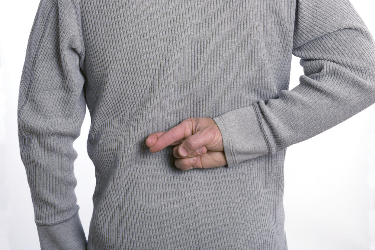 Horizontal back view of crossed fingers. Gray shirt cropped at the waist and the shoulders.