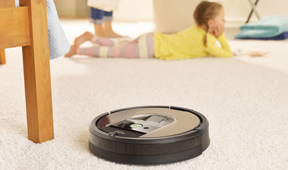 Roomba next to a chair leg, with a child on the carpet in the background.