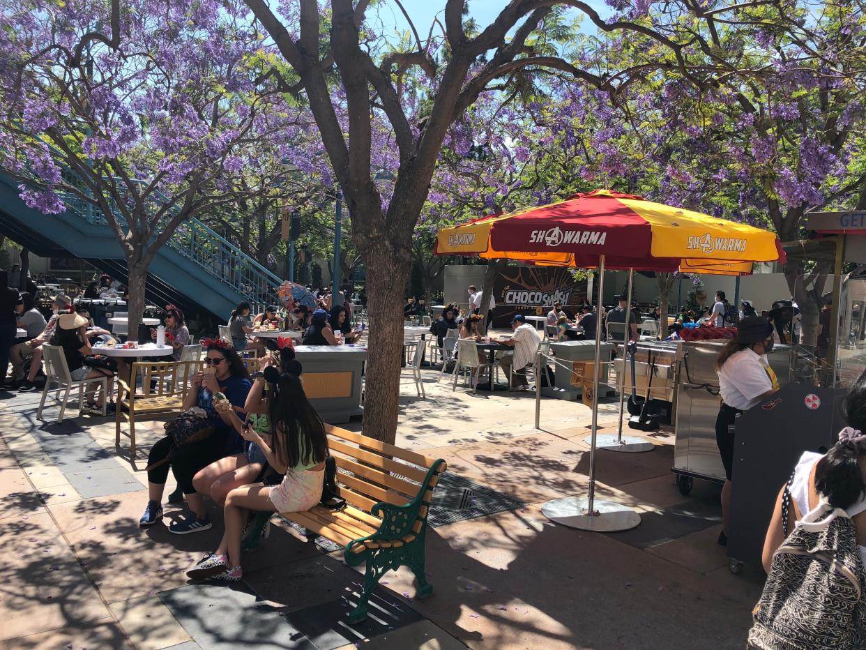 People sitting on benches and eating outside at Disneyland near purple trees