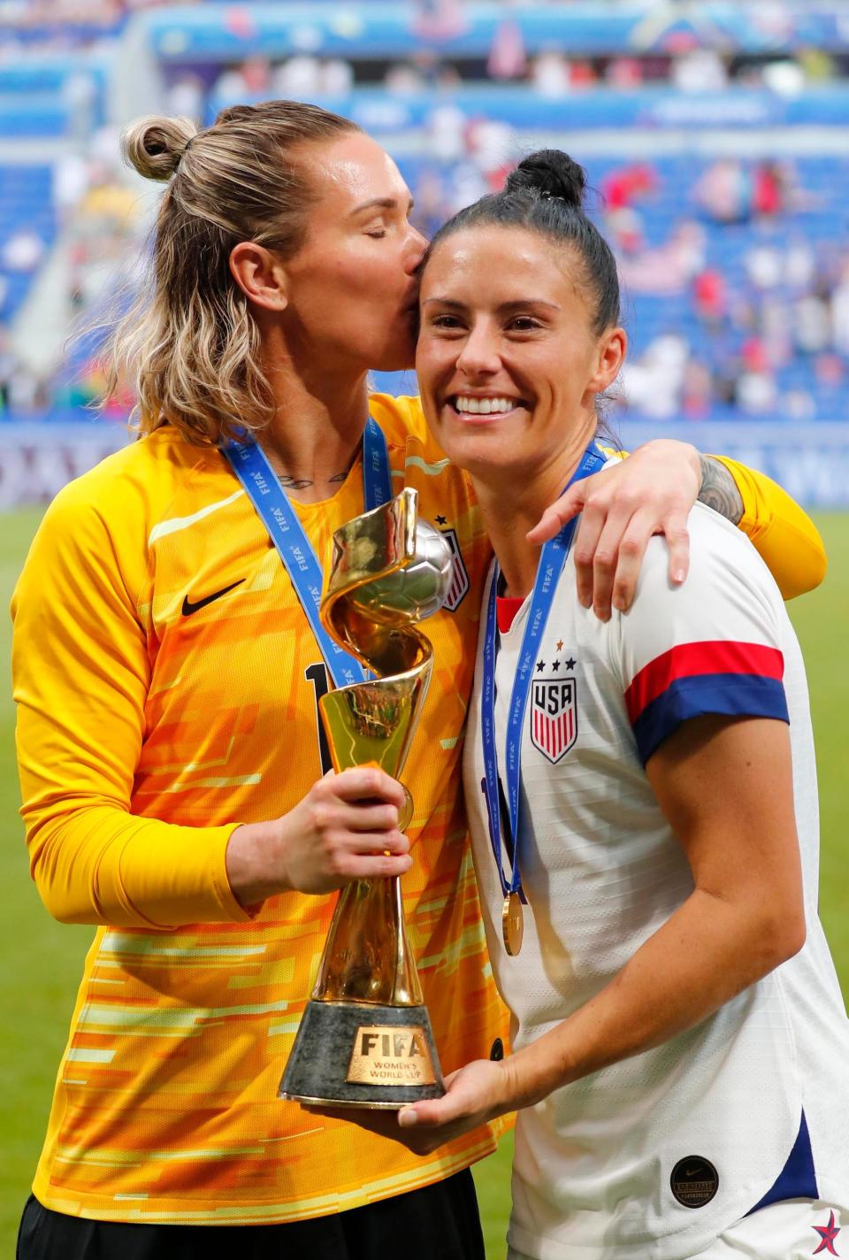 Ashlyn Harris (left) kisses Ali Krieger as they pose with the 2019 World Cup trophy.