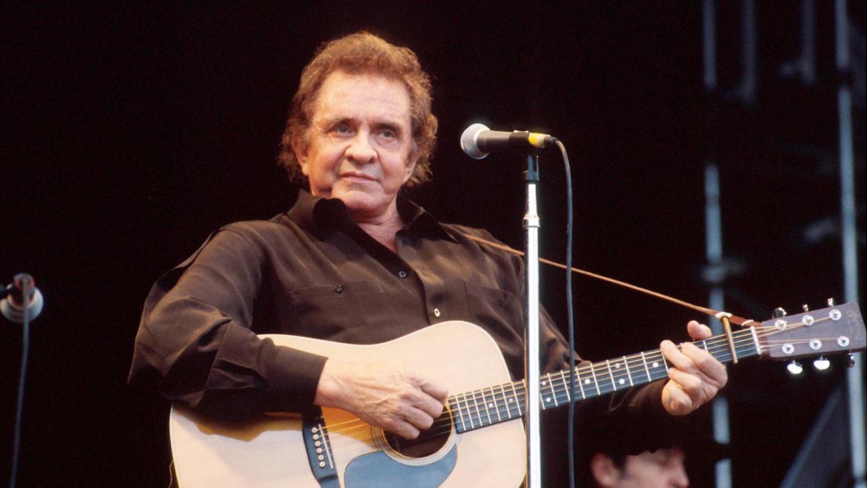 johnny cash wearing a black shirt and playing a guitar on stage during a concert performance