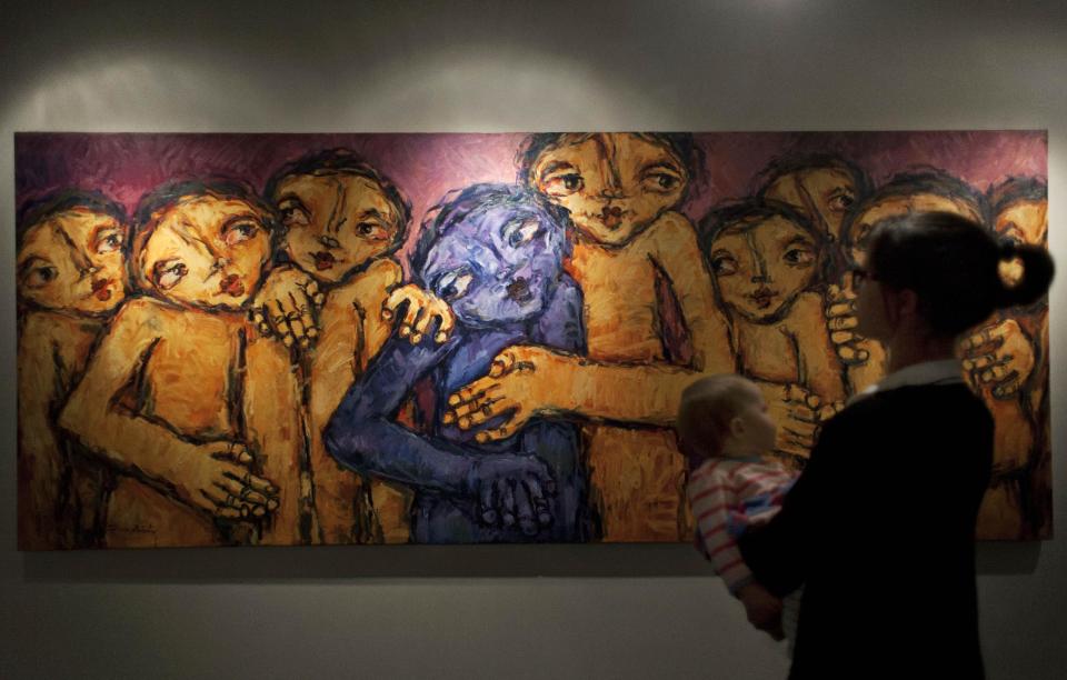 In this photo taken Saturday, May 10, 2014, a woman carrying her child, stands in front of an oil on canvas painting named The Bitter and the Bitterness, by Palestinian artist Raouf al-Ajouri, during an art exhibition "Traces, a testimony to memory," displaying over forty Palestinian artists work from Gaza, in the West Bank city of Ramallah. Fifty-three paintings and two sculptures by 45 artists have gone on display in the West Bank city of Ramallah, said Haneen Qatamesh, a spokeswoman for one of the sponsors, the Palestinian company PADICO. Since Saturday's opening, 12 works have been sold for prices ranging from $850 to $9,000, she said. (AP Photo/Nasser Nasser)