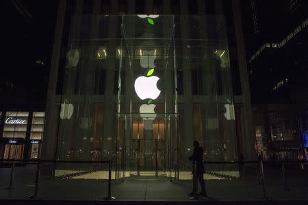 An employee stands in front of the Apple flagship store on 5th Avenue in New York April 22, 2015. The leaf on the Apple logo was tinted green after midnight in honor of Earth Day at Apple's 24hr store. REUTERS/Brendan McDermid