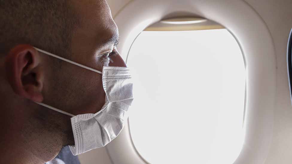 Hombre con mascarilla junto a la ventanilla del avión