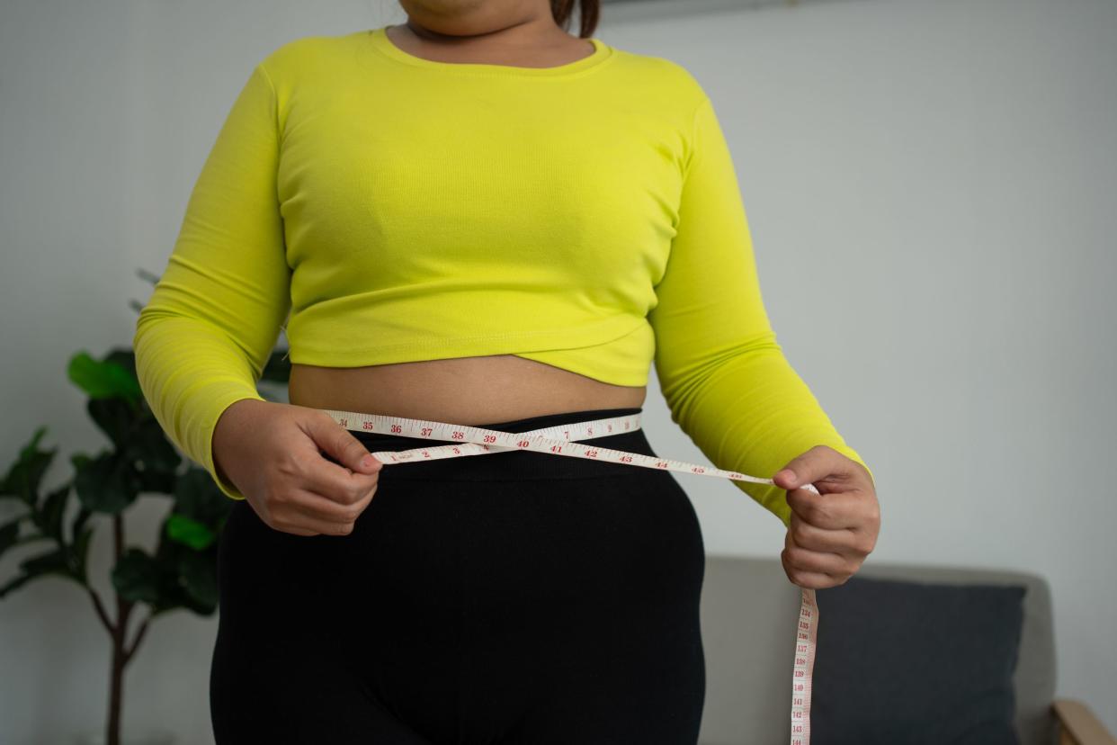 Overweight woman using a tape measure around waist and belly fat, Fat Asian woman workout at home. Concept of healthy, food for health and lifestyle, weight loss