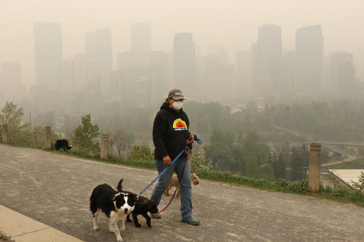 Wearing a protective mask, a dog walker ventures out as heavy smoke from northern Alberta forest fires blankets downtown Calgary on May 16, 2023. THE CANADIAN PRESS/Larry MacDougal