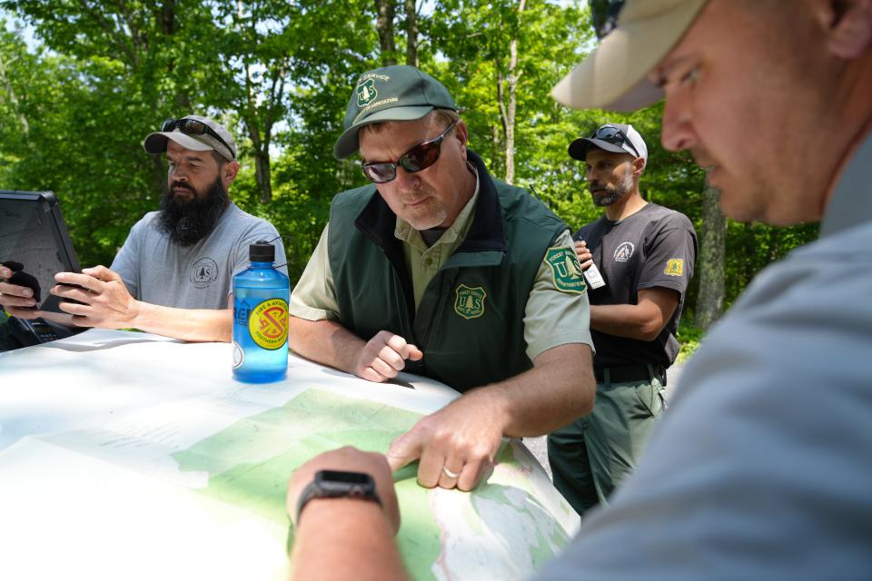 Forest Service worker David Whitmore (center) consults a map with Augusta county emergency management worker Patrick Lam (right) along with Aaron Bennington (left)  and Brent Foltz rear) on June 5, 2023.  Members of the U.S. Forest Service and Augusta County emergency management work Monday afternoon near an old trail that leads to a crash site.   An unresponsive pilot collided into mountainous terrain near the George Washington National Forest Sunday. F-16 fighter jets tried to alert the pilot with flares and traveled at supersonic speeds.