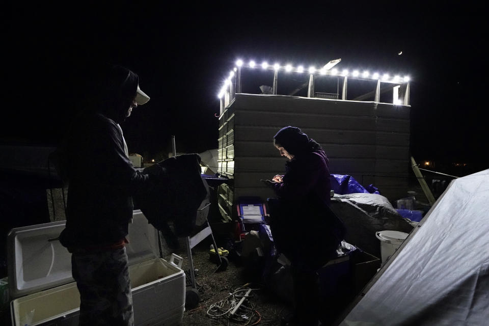 Cristin Trahan checks her calendar on her phone as she discusses upcoming food distribution events with her husband Ricky Trahan, in Lake Charles, La., Thursday, Dec. 17, 2020. They were hit by Hurricanes Laura and Delta. She, Ricky and a son are living in tents on the property of their destroyed home, while her other son, his fiancée and their one-year old son are living in a loaned camper there. A relative's home on the same property is now gutted and they are living in a camper as well. (AP Photo/Gerald Herbert)