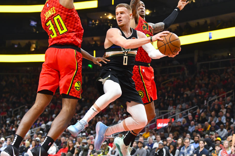 Milwaukee Bucks guard Donte DiVincenzo (0) splits the defense of Atlanta Hawks center Damian Jones (30) and forward John Collins as he looks to pass during the first half of an NBA basketball game Friday, Dec. 27, 2019, in Atlanta. (AP Photo/John Amis)