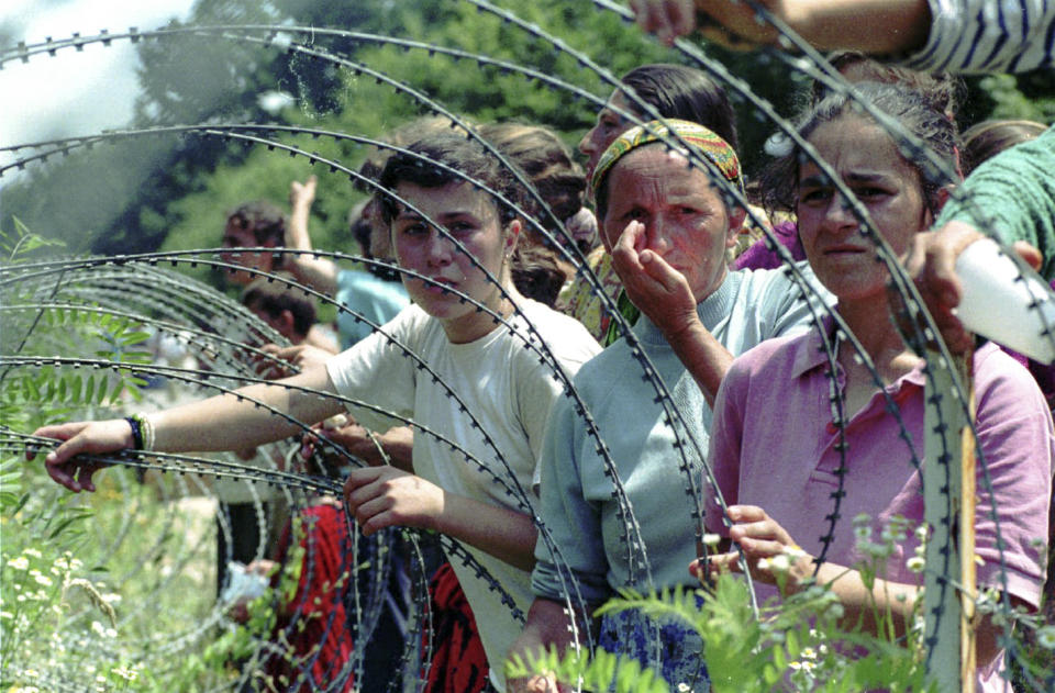 FILE- In this Thursday, July 13, 1995, file picture, refugees from Srebrenica look through the razor-wire at a UN base, outside Tuzla. Survivors of the genocide in the eastern Bosnian town of Srebrenica, mainly women, will on Saturday July 11, 2020, commemorate the 25th anniversary of the slaughter of their fathers and brothers, husbands and sons. At least 8,000 mostly Muslim men and boys were chased through woods in and around Srebrenica by Serb troops in what is considered the worst carnage of civilians in Europe since World War II. The slaughter was also the only atrocity of the brutal war that has been confirmed an act of genocide.(AP Photo/Darko Bandic, File)