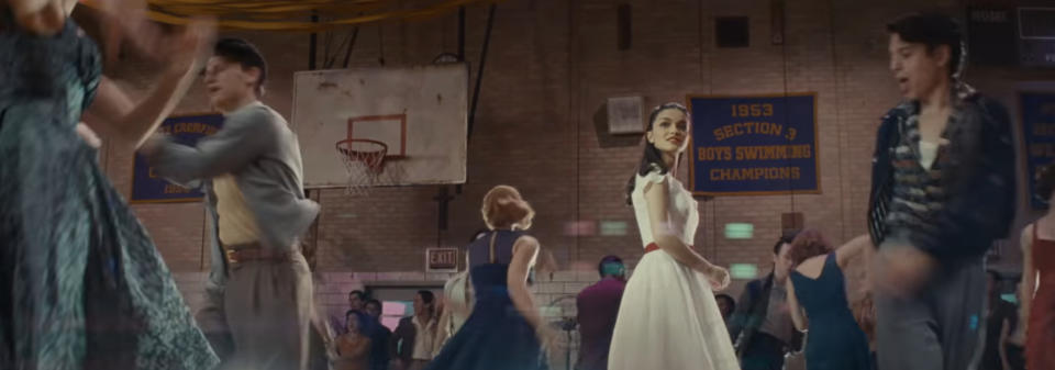 A scene from "West Side Story" depicting a high school dance, with characters dancing in 1950s attire. Banners for swimming champions hang in the background