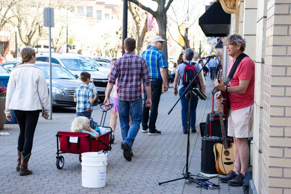 People walking down the street in downtown Holland with a man playing a guitar and singing against a wall