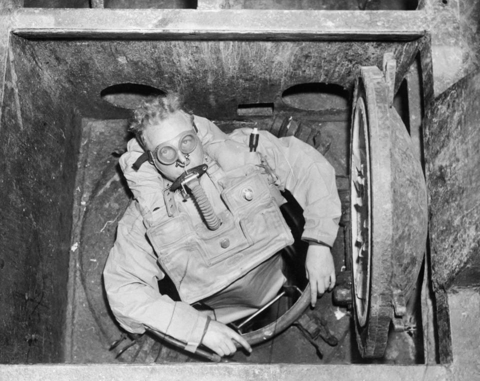 A Royal Navy diver enters a submarine escape hatch in the 1950s