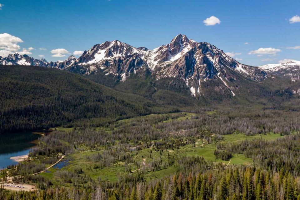 <p>Getty</p> Deep green forest blankets meadows laying below a mountain peak.