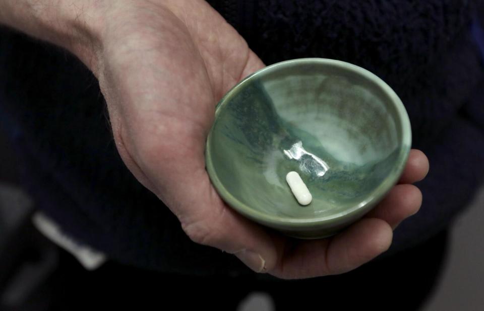 A hand holds a bowl containing a psilocybin pill