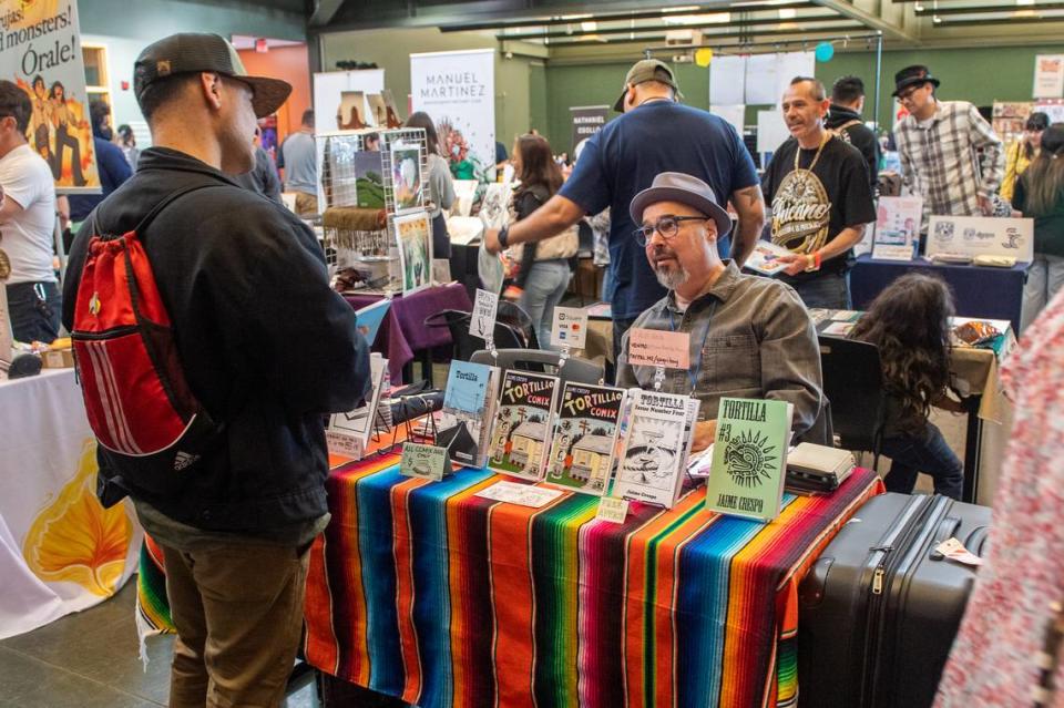 El artista Jaime Crespo conversa con un visitante de su mesa en el 2023 Latinx Comics Art Festival de Modesto. www.latinxcomicartsfest.com